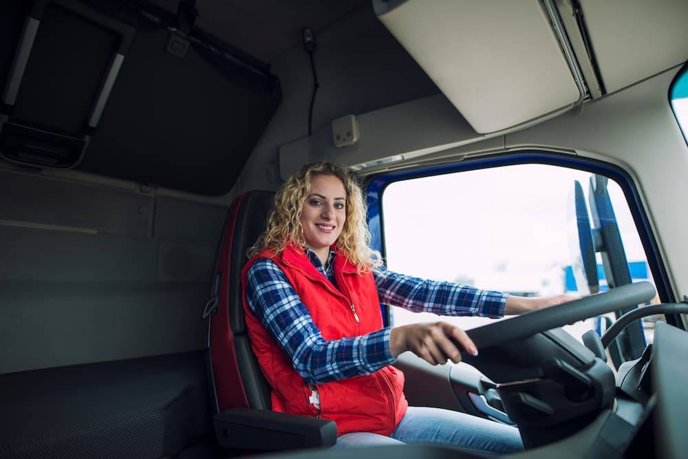A woman sits in the driver seat of a commercial shipping truck